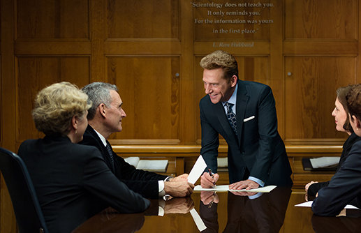 David Miscavige leading a conference room meeting with an L. Ron Hubbard quote on the wall behind him.